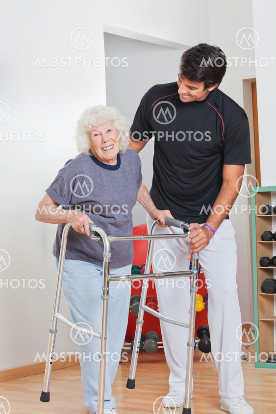 Senior Woman Holding Walker While Trainer Assisting Her
