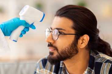 Unrecognizable doctor in protective suit measuring body...