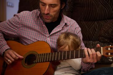 Father and Child Playing Guitar Together Indoors