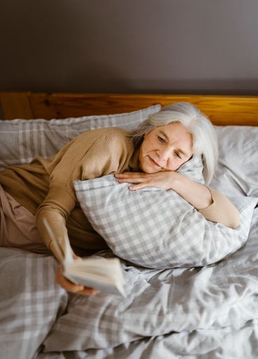 Senior woman reading book while lying on bed at home
