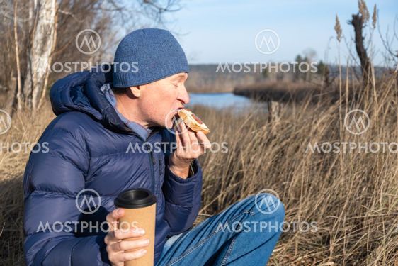 A man sits on the grass in the fall and eats a cheese...