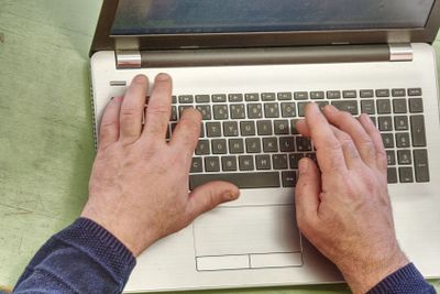 Working on laptop close up of hands of old man. 