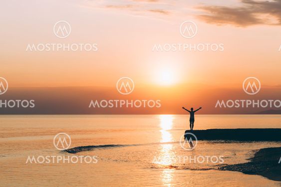 Young woman standing with raised arms in sunset