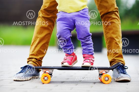 Toddler girl learning to skateboard with her father