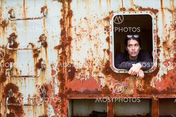Portrait of a young woman in the window of an abandoned iron rusty object.