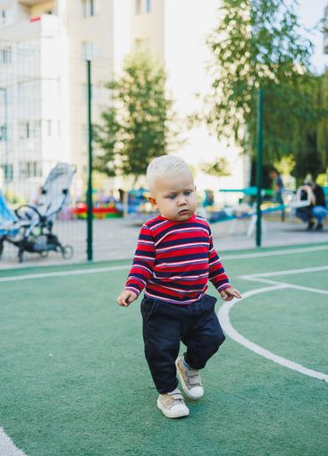 A fair-haired one-year-old boy in jeans and sneakers...