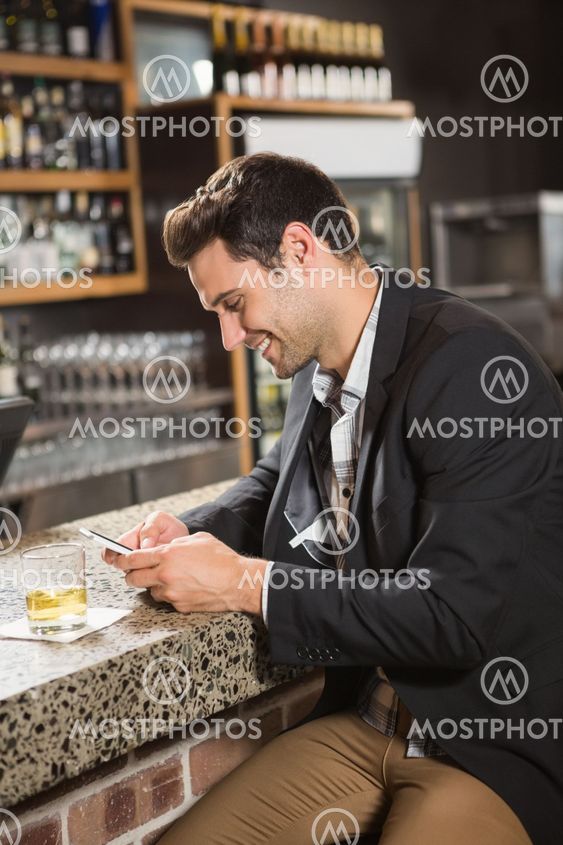 Handsome man having a whiskey and using smartphone