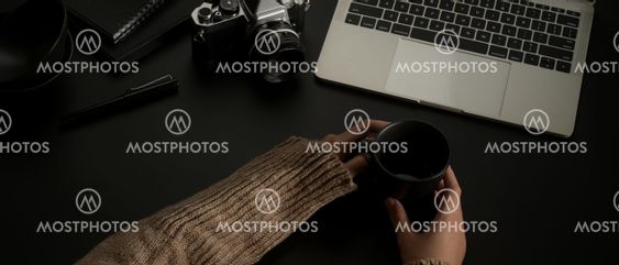 Female hands holding coffee mug on dark office desk with...