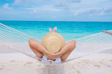 A young woman in a straw hat has her hands behind her...