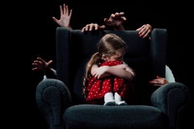 scared child sitting in armchair surrounded with human...