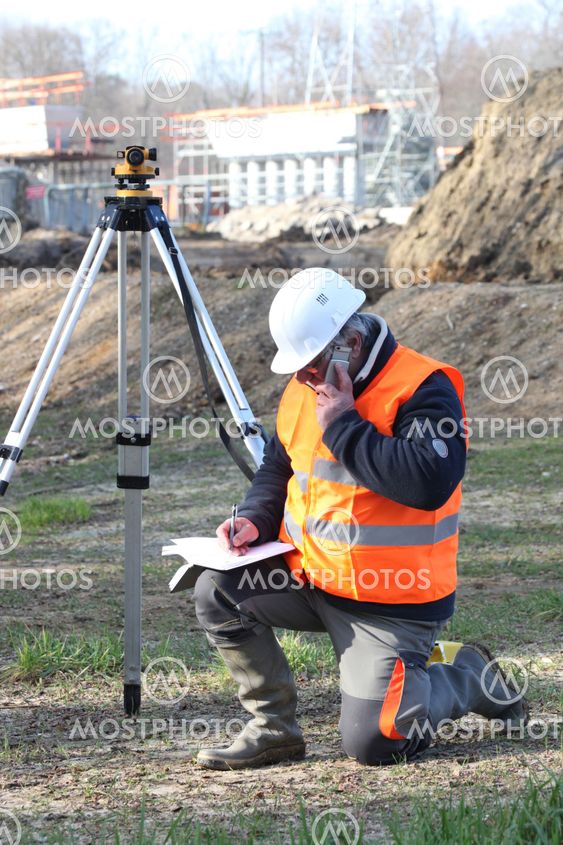 A land surveyor writing in his notebook while talking on the phone