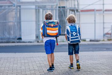 Two little kid boys with satchels. Schoolkids on the way...
