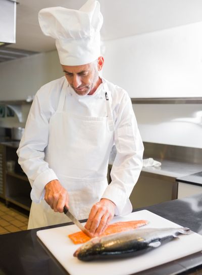Concentrated male chef cutting fish in kitchen