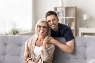Happy mature mother sit on sofa in grownup son embraces