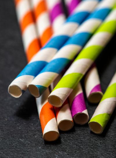 Multicoloured drink straws on dark stone background....