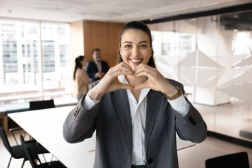 Happy beautiful young businesswoman making hand heart...