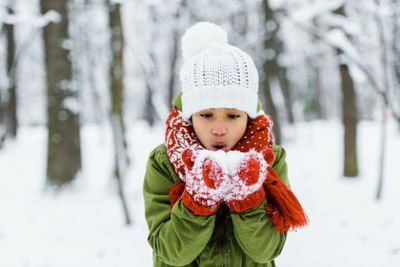 cute african american child blowing snow in winter forest