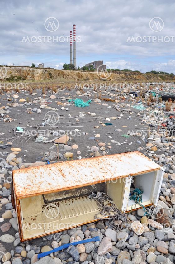 Trashed fridge on the seashore next to a factory
