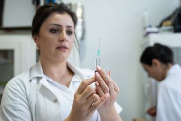 A focused nurse in a white lab coat carefully prepares a...