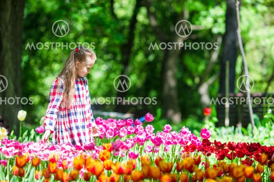 Little adorable girl with flowers in tulips garden