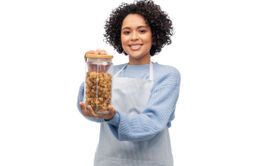 smiling woman in apron holding jar with pasta