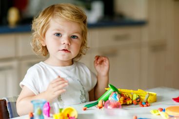 Adorable cute little toddler girl with colorful clay at...
