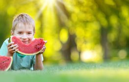Cute child lying on the grass and eating juicy slice of...