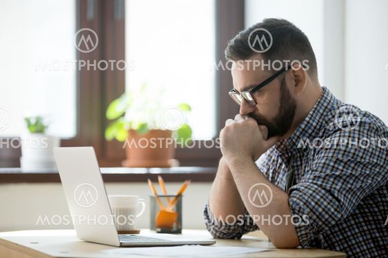 Millennial casual businessman thinking and looking at laptop in