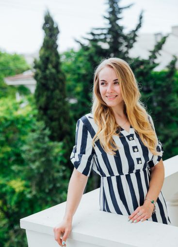 blonde woman in summer striped dress smiling on balcony