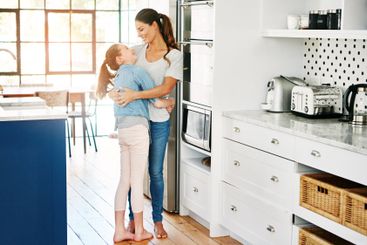 Girl, mom and happy with hug in kitchen for motherhood,...
