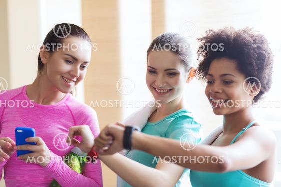 happy women showing time on wrist watch in gym