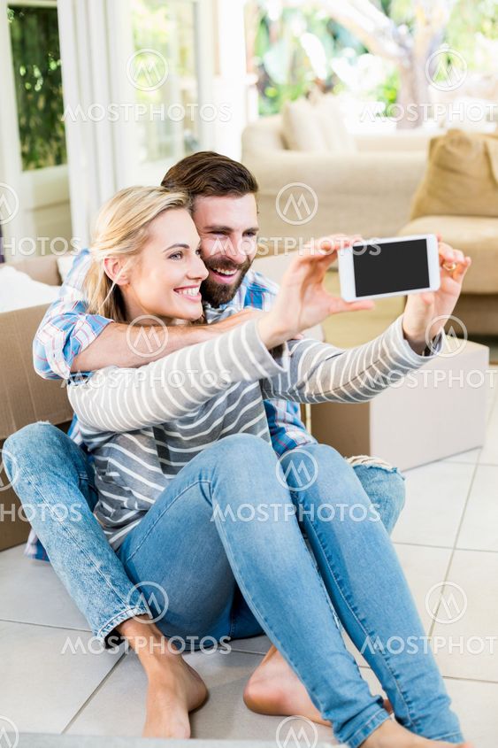 Couple sitting on floor and taking selfie in living room