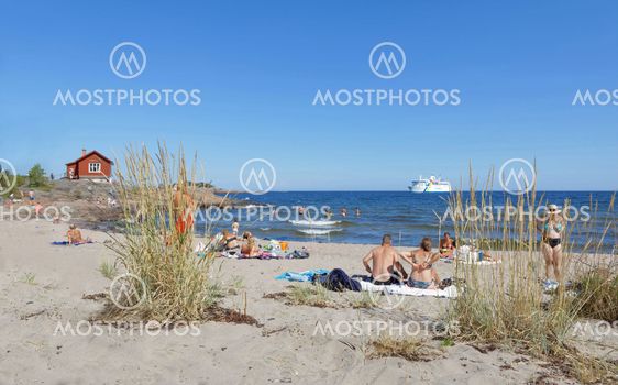 People relaxing on the beach watching a ferry, blue sky...