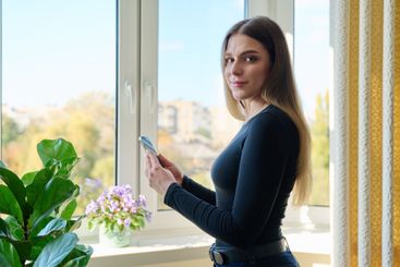 Confident young woman with smartphone in home interior