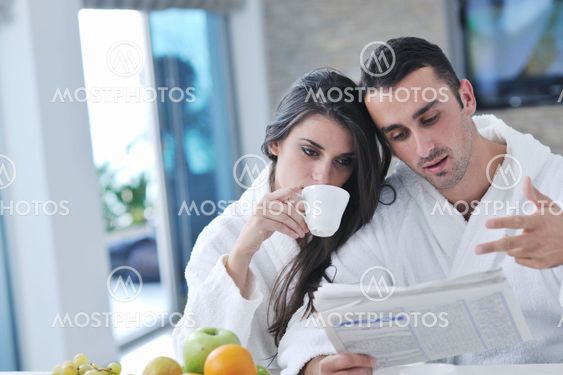 Happy couple reading the newspaper in the kitchen at breakfast