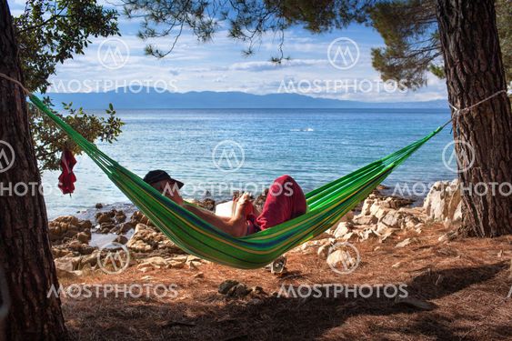 Man läser bok i hängmatta på strand