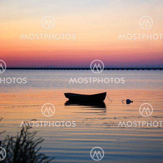 Lone rowboat in calm water at sunset