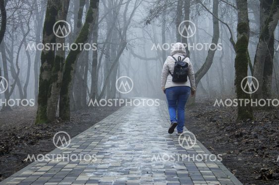 Lonely adult woman walking in autumn park in mysty morning