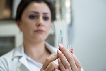 A focused nurse in a white lab coat carefully prepares a...