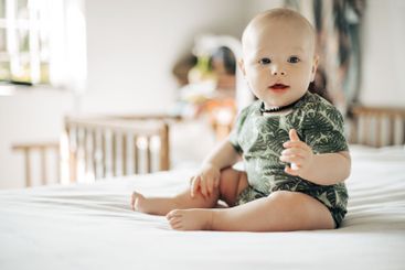 Baby boy, bed and smile in home with excited face,...