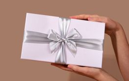 Woman holding white gift box with silver ribbon bow on...