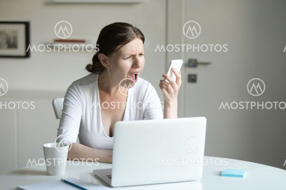Portrait of a woman at desk with laptop, looking at the mobile