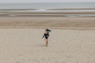 attractive young woman in black bodysuit running on sandy...