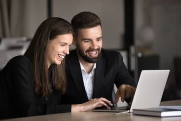 Two Caucasian teammates using laptop in modern office