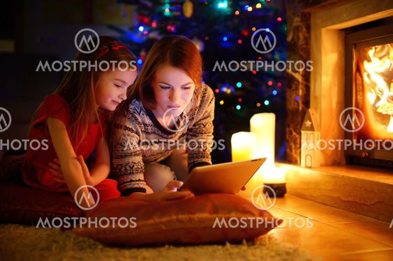 Mother and daughter using a tablet by a fireplace on...