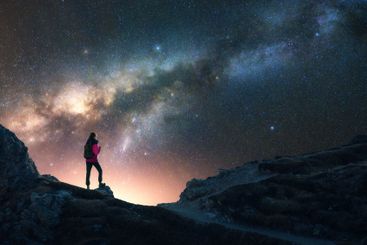 Glowing Milky Way and woman on mountain peak at starry...