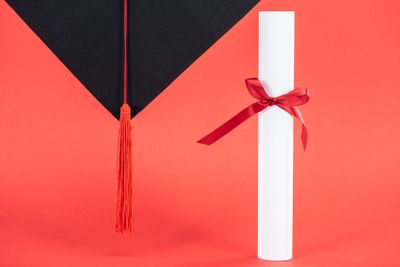 Academic cap with tassel and diploma with ribbon on red...