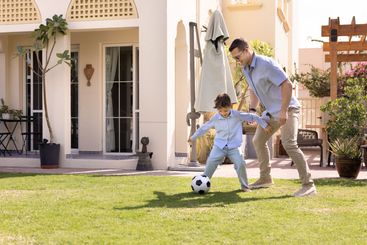 Active dad and sporty son boy playing soccer on backyard