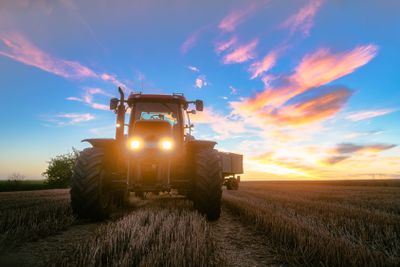 Tractor on harvested grain field during dusk
