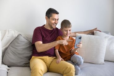 Father and son engaging with smartphone sitting together...